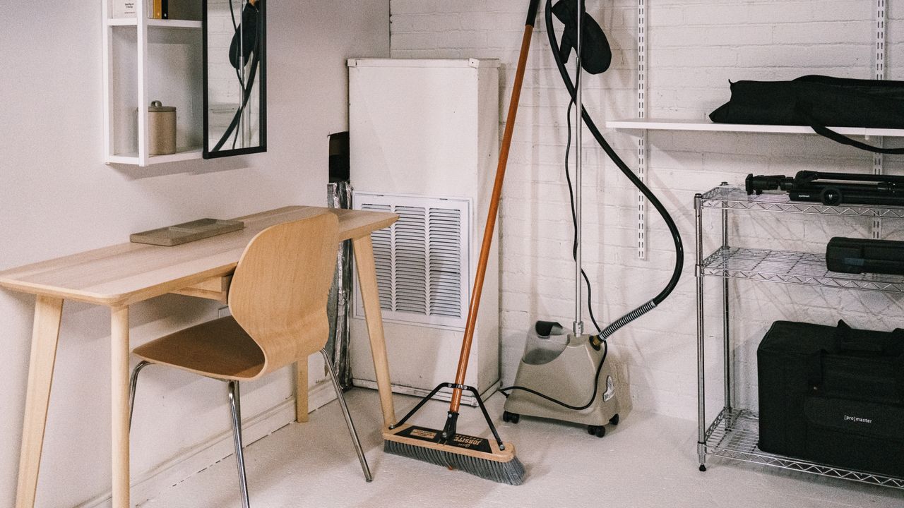 hero-img-01 A tidy home office space featuring a wooden desk, chair, broom, and cleaning equipment.